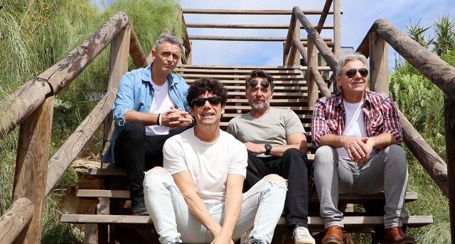 Los Cucas sentados en unas escaleras de madera junto a la playa