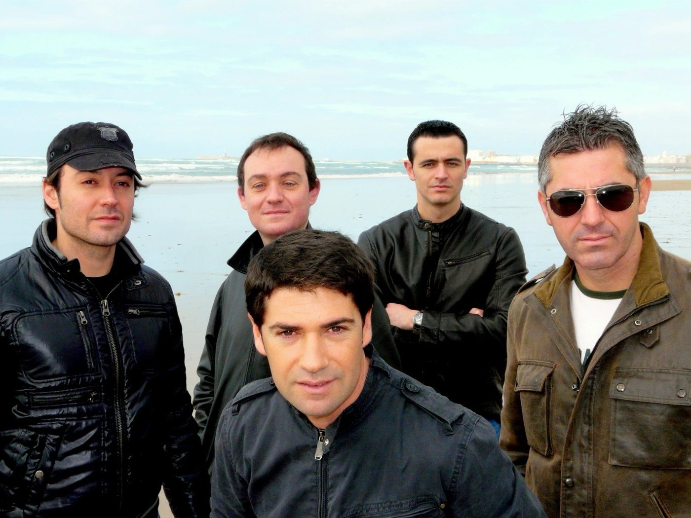 Los cinco miembros de Los Cucas en la playa, con el mar y la ciudad al fondo